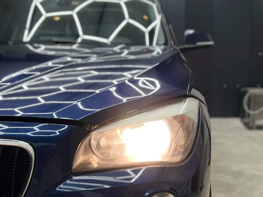 BMW X1 albastru înainte: far aprins cu lumină galbenă de halogen