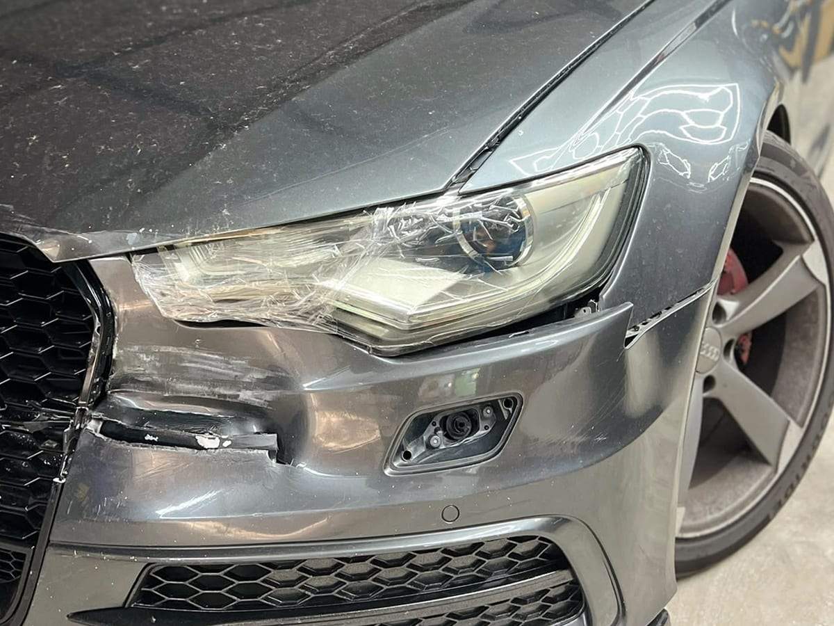 Audi A6 gri înainte: sticla farului spartă, acoperită cu folie